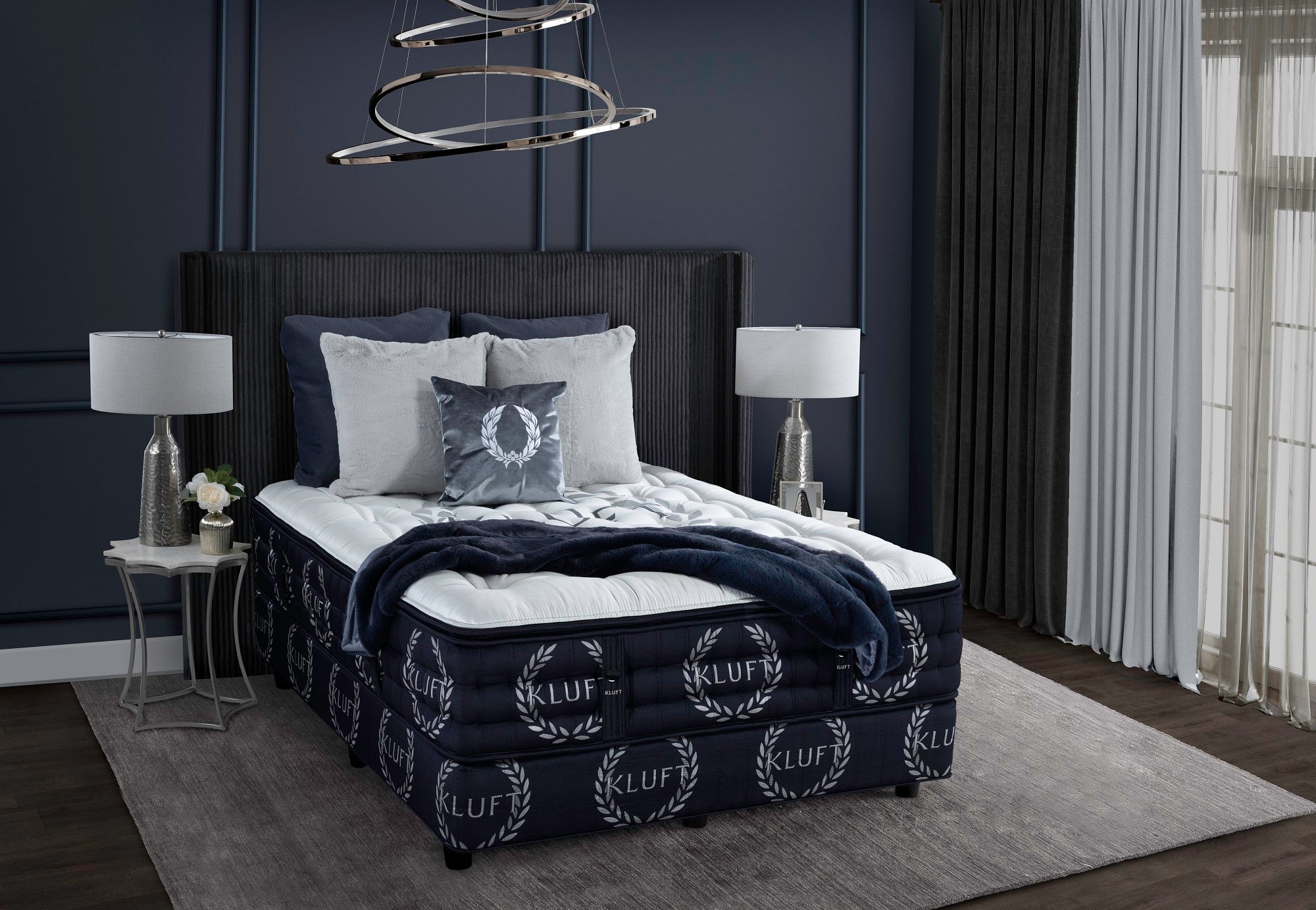 Bedroom with a bed featuring a KLUF branded comforter against a dark wall.